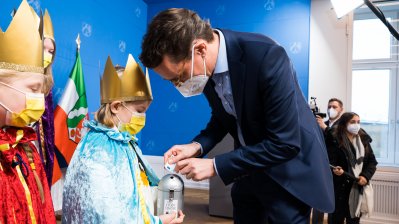 Ministerpräsident Hendrik Wüst steckt Geldscheine in eine Gelddose