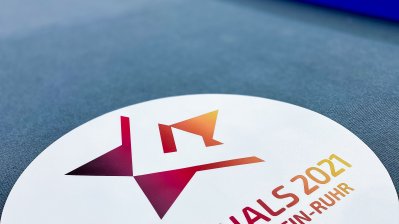 Auf dem Boden liegt das weiße, kreisrunde Logo mit dem Text "Die Finals 20210Berlin Rhein-Ruhr" und dem Finals-Stern oben rechts in Rot und Orange.