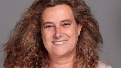 eine Frau mit offenen Haaren, Bluse und Blazer lächelt frontal in die Kamera