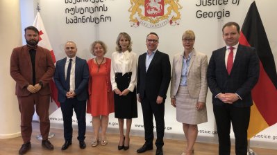 vier Männer und drei Frauen stehen vor einer Wand mit dem georgischen Wappen und einer Deutschland-Fahne