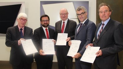 Die Vertreter schauen in die Kamera und halten jeweils den Kooperationsvertrag in den Händen