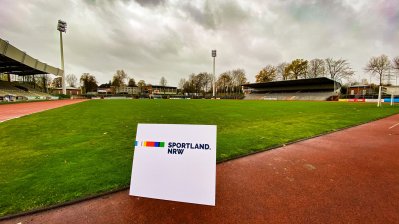 Man schaut über die grüne Rasenfläche des Lohheidestadions, um die Rasenfläche herum eine rote Tartanbahn. Links befinden sich die überdachten Tribünen.