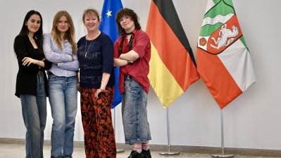 vier Frauen, davon drei mit verschränkten Armen, stehen vor den Flaggen von Europa, Deutschland und NRW 