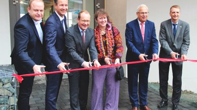 Staatssekretärin Andrea Milz und andere beim Durchschneiden des roten Einweihungsbandes des neuen Funktionsgebäudes der Bobbahn.
