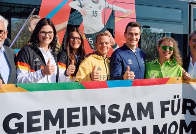 Gruppenfoto vor der Straßenbahn mit dem angeschnittenen Schriftzug "Gemeinsam für größten Mom"