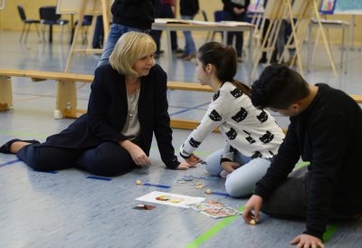 Ministerpräsidentin Hannelore Kraft sitzend auf dem Turnhallenboden mit Schülerinnen und Schülern mit Themenpuzzle 