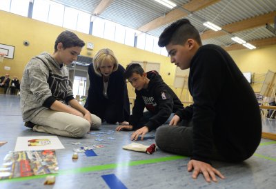 Ministerpräsidentin Hannelore Kraft sitzend auf dem Turnhallenboden mit Schülerinnen und Schülern mit Themenpuzzle 