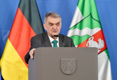 Minister Reul spricht an einem Rednerpult vor Flaggen