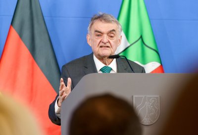 Minister Reul spricht an einem Rednerpult vor Flaggen