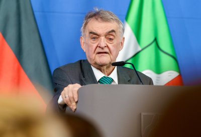 Minister Reul spricht an einem Rednerpult vor Flaggen