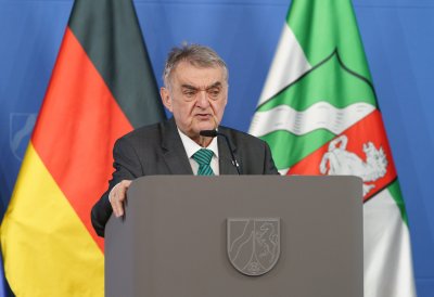 Minister Reul spricht an einem Rednerpult vor Flaggen