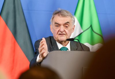 Minister Reul spricht an einem Rednerpult vor Flaggen