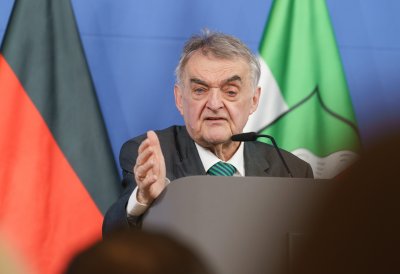 Minister Reul spricht an einem Rednerpult vor Flaggen