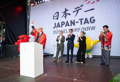 Ein Mann in traditionell japanischer Kleidung hält auf der Bühne einer Ansprache