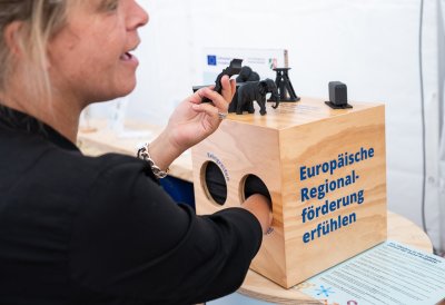 Wirtschaftsministerin Mona Neubaur fasst in eine Holzbox mit dem Schriftzug "Europäische Regionalförderung erfühlen"