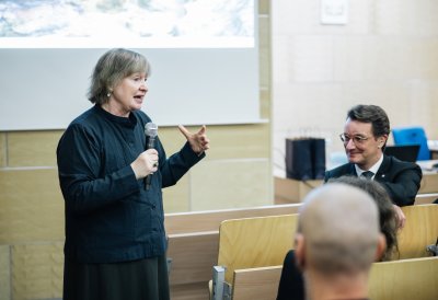 Eine vortragende Person erzählt etwas im Hörsaal, rechts sitzt MP Wüst