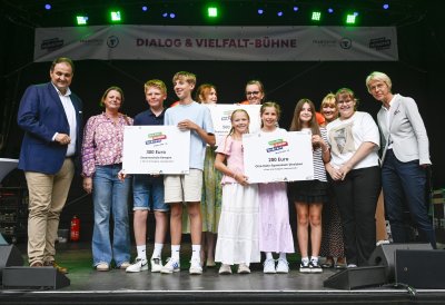 Ministerin Feller und eine Schulgruppe posieren für ein Foto auf einer Bühne