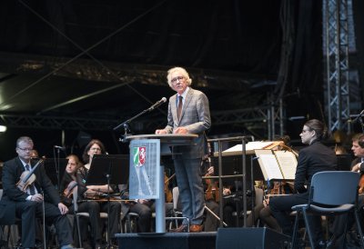 Der Minister steht am Rednerpult, hinter ihm sitzen Musiker des Orchesters