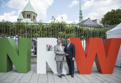 Herr Laschet und Herr Kufen stehen vor großen NRW-Buchstaben
