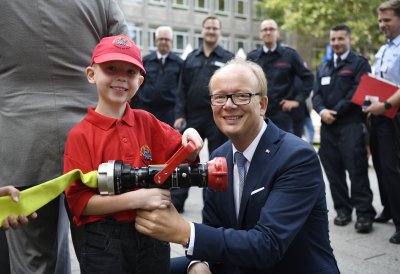 Landtagspräsident André Kuper und ein junger Feuerwehrmann halten einen Feuwehrschlauch