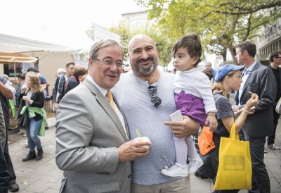 Ministerpräsident Armin Laschet mit Eis in der Hand und ein Vater mit Kind auf dem Arm posieren für ein Foto