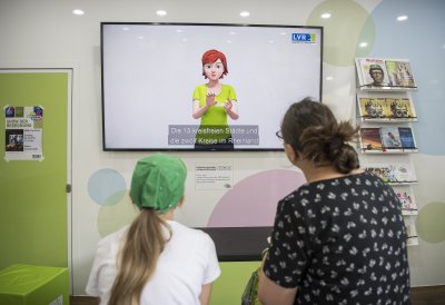 Eine Mutter schaut mit ihrer Tochter auf einen Monitor, auf dem die 13 kreisfreien Städte des Rheinlands erklärt werden