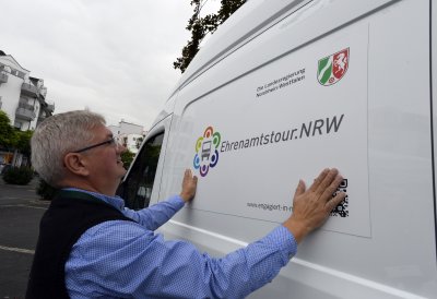 Ein älterer Herr beklebt den Ehrenamtstourbus seitlich mit dem Ehrenamtstour.NRW-Log