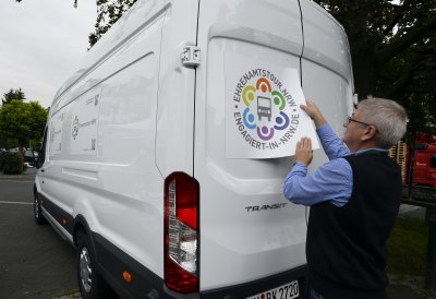 Ein älterer Herr beklebt den Ehrenamtstourbus hinten mit dem Ehrenamtstour.NRW-Logo.