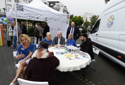 Ehrenamtstour-Veranstaltung: Eine Gruppe sitzt an einem runden Tisch, rechts steht der Ehrenamtstourbus, hinten steht ein Pavillonzelt.