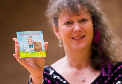 Staatssekretärin Andrea Milz hält das Pixi-Buch mit ihrer rechten Hand vor sich für die Kamera.