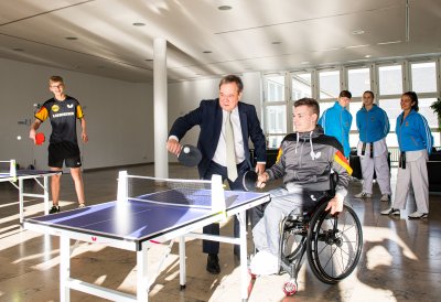 Armin Laschet spielt mit einem jungen Sportler im Rollstuhl Tischtennis.