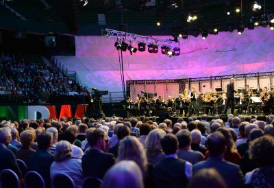 Der Dirigent steht auf der Bühne, im Hintergrund das Orchester, im Vordergrund Köpfe des Publikums
