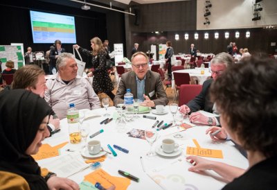 Sieben Menschen sitzen im Gespräch an einen runden Tisch.