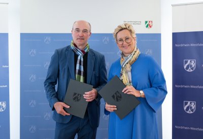 vor einem blau-weißen Roll-Up der Landesregierung NRW stehen links Prof. Dr. Ulrich Rüdiger, Rektor RWTH Aachen und neben ihm Prof. Dr. Tamara Appel, Rektorin der FH Dortmund