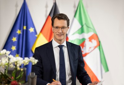 Ministerpräsident Hendrik Wüst sitzt vor Flaggen am Schreibtisch