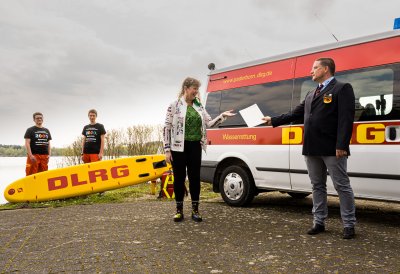 Eine Frau überreicht vor einem Rettungswagen eine Urkunde an einen Mann des DLRG