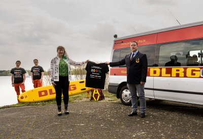 Ein Mann und eine Frau halten ein Tshirt hoch, im Hintergrund stehen zwei weitere Männer neben einem Rettungswagen