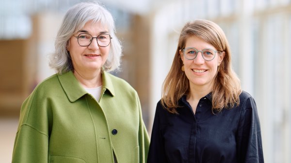 Petra Ladenburger, eine ältere Frau mit grauen schulterlangen Haaren und einer runden Brill in grünem Kostüm steht links neben Verena Schäffer in einem schwarzen Hemd