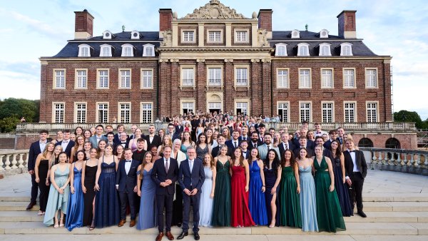 Große Gruppe festlich gekleideter Menschen posiert auf den Treppen vor der prächtigen Backsteinfassade von Schloss Nordkirchen.