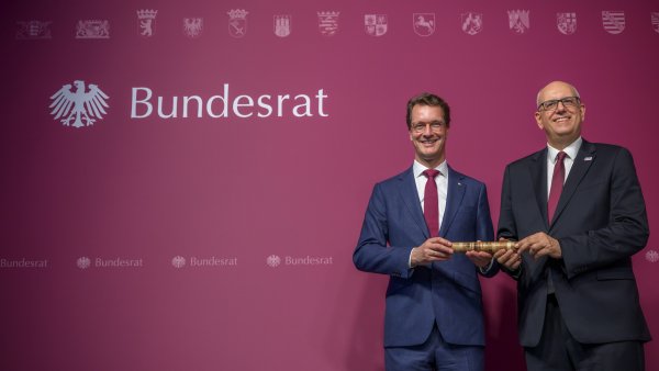Zwei Männer in Anzügen halten gemeinsam einen Holzstab fest.