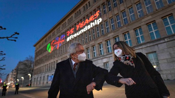 Der Minister und die Botschafterin begrüßen sich mit Corona-Gruß vor dem Behrensbau