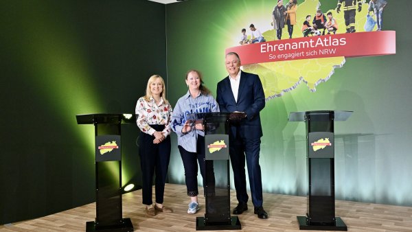 zwei Frauen und ein Mann stehen hinter drei Pulten vor einer grünen Leinwand mit einem EhrenamtAtlas Schriftzug