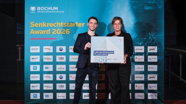 Zwei Personen präsentieren gemeinsam den „Senkrechtstarter Award 2026“ vor einer Sponsorenwand mit Logos und der Aufschrift „BOCHUM Wirtschaftsentwicklung“. Rechts ist Ministerin Mona Neubaur zu sehen.