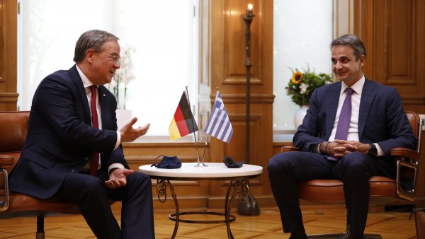 Zwei Männer sitzen neben einem Tisch auf dem eine Fahne von Deutschland und Griechenland stehen