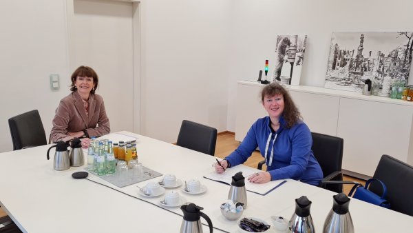 Staatssekretärin Andrea Milz in blauer Strickjacke sitzt mit einer Dame der Stadt Köln an einem Tisch.