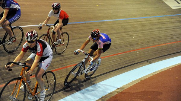 Vier Bahnradfahrer auf einer Indoor-Bahnstrecke im Wettkampf.