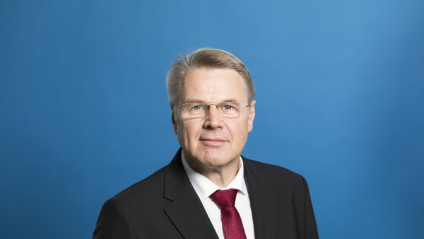 Staatssekretär Bottermann freundlich lächelnd - Hintergrund blau.