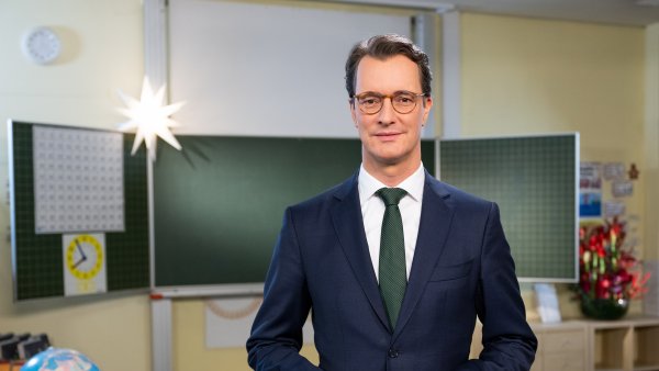 Ministerpräsident Hendrik Wüst steht in einem Klassenraum und spricht in die Kamera