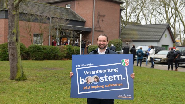 Ein man hält ein Plakat der Booster-Impfkampagne hoch