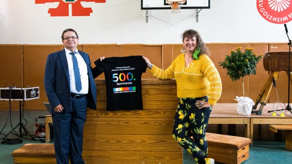 Staatssekretärin MIlz hält ein schwarzes T-Shirt mit Logo der Förderung mit der Zahl 500 in Regenbogenfarben.